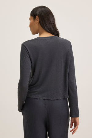 A person with long dark hair is seen from the back, wearing Velvet by Graham & Spencer's KARA LINEN KNIT TEE, a dark gray long-sleeve top paired with matching cropped pants, standing against a plain background.