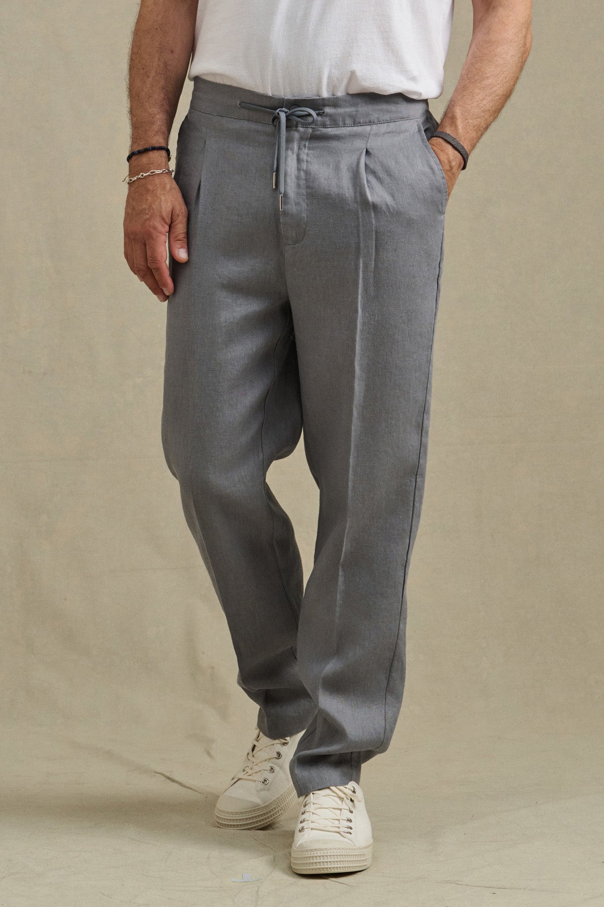 A person wearing the ELLIOTT PANT by Velvet by Graham & Spencer, paired with a white t-shirt, white sneakers, and bracelets stands against a neutral background.-41479915667649