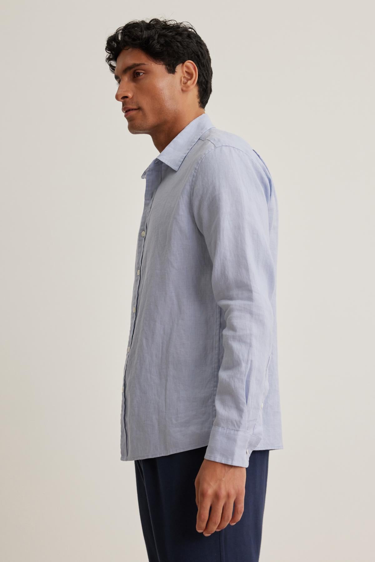   Man in a CARUSO LINEN BUTTON-UP SHIRT from Velvet by Graham & Spencer, paired with dark pants, stands looking left against a plain background. 