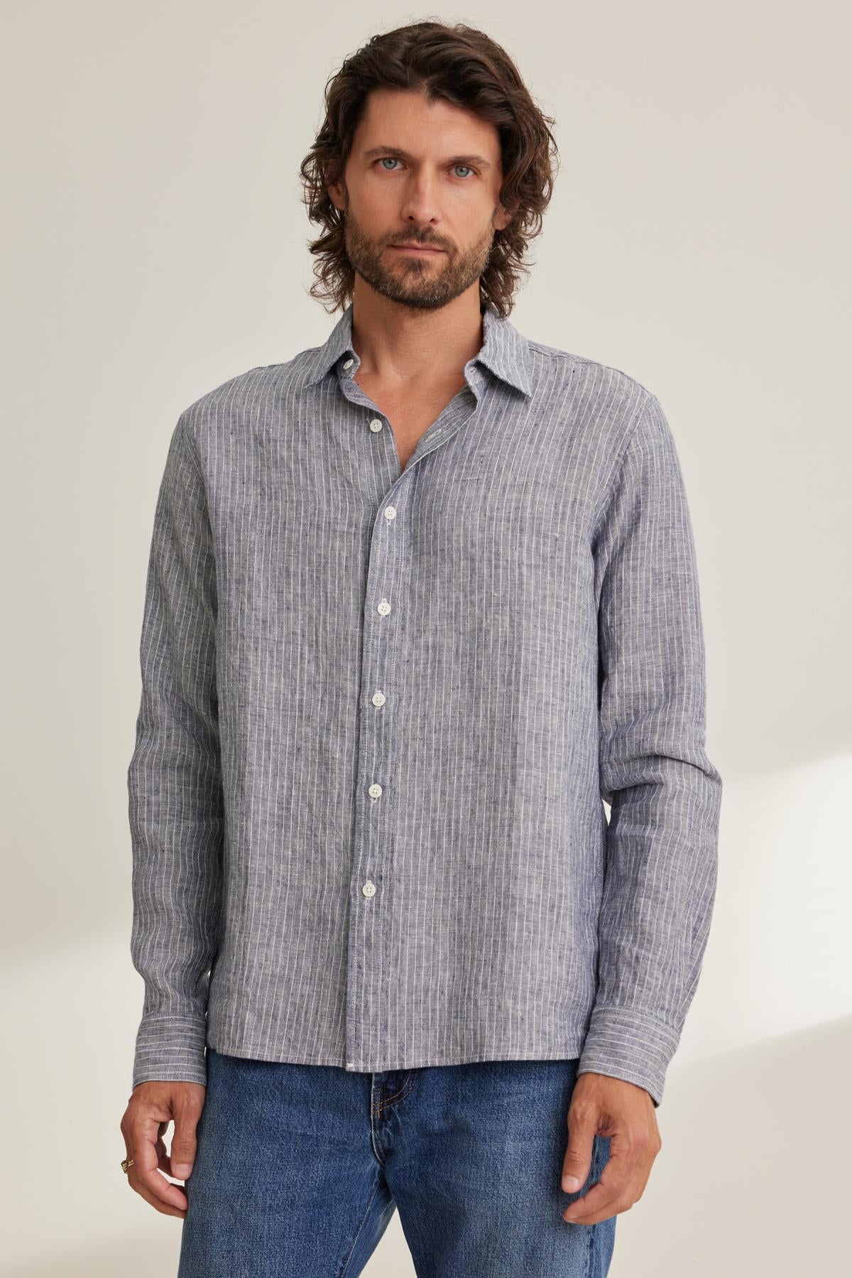   Man wearing a CARUSO LINEN BUTTON-UP SHIRT by Velvet by Graham & Spencer and blue jeans, standing against a light background. 