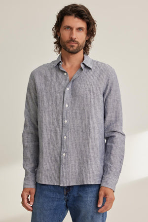 Man wearing a CARUSO LINEN BUTTON-UP SHIRT by Velvet by Graham & Spencer and blue jeans, standing against a light background.