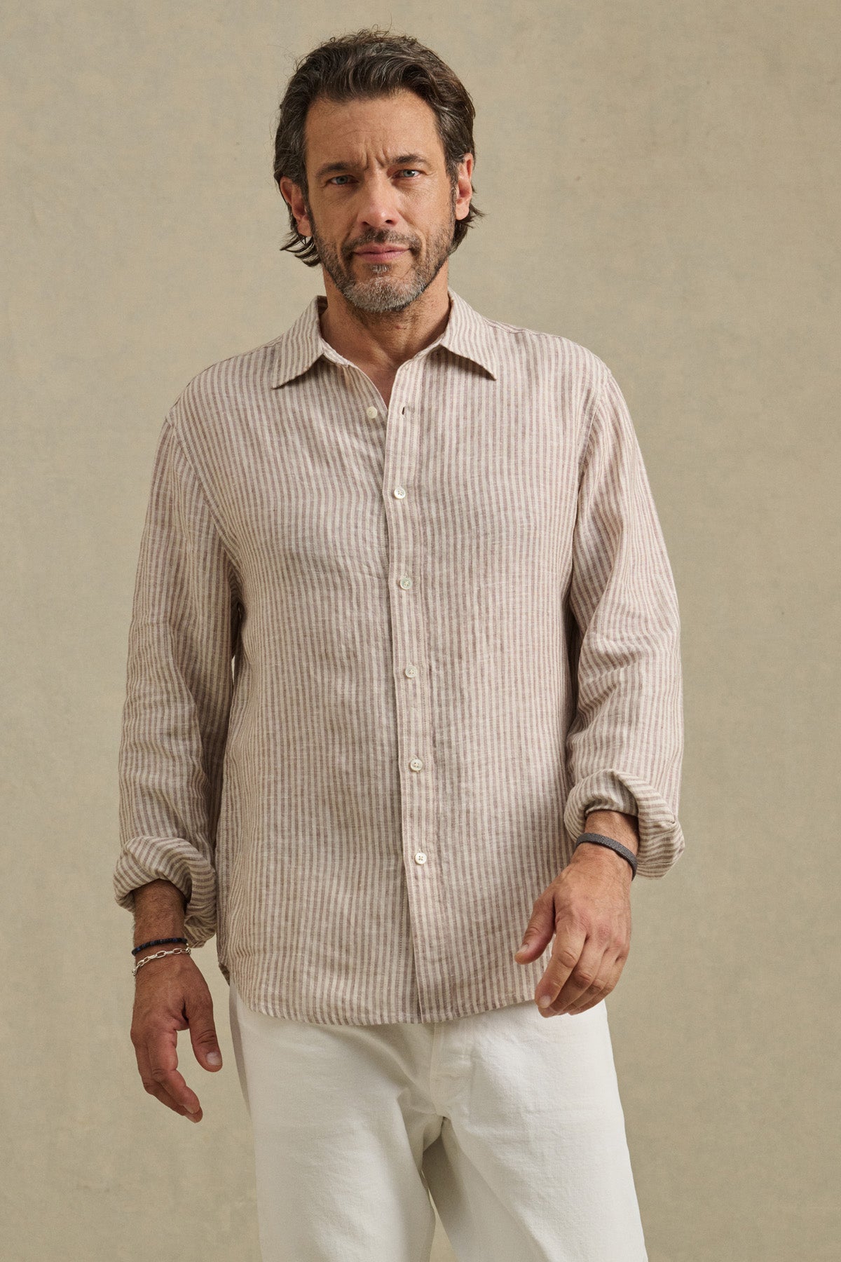 A man stands against a plain background wearing the CARUSO LINEN SHIRT by Velvet by Graham & Spencer, featuring beige and white stripes, paired with white pants.-41145256902849
