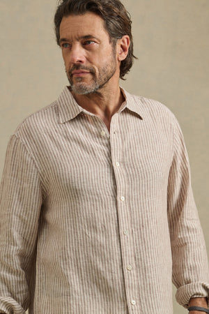 Man wearing the CARUSO LINEN SHIRT by Velvet by Graham & Spencer, a beige and white striped long-sleeve button-up, looking to the side against a plain background.