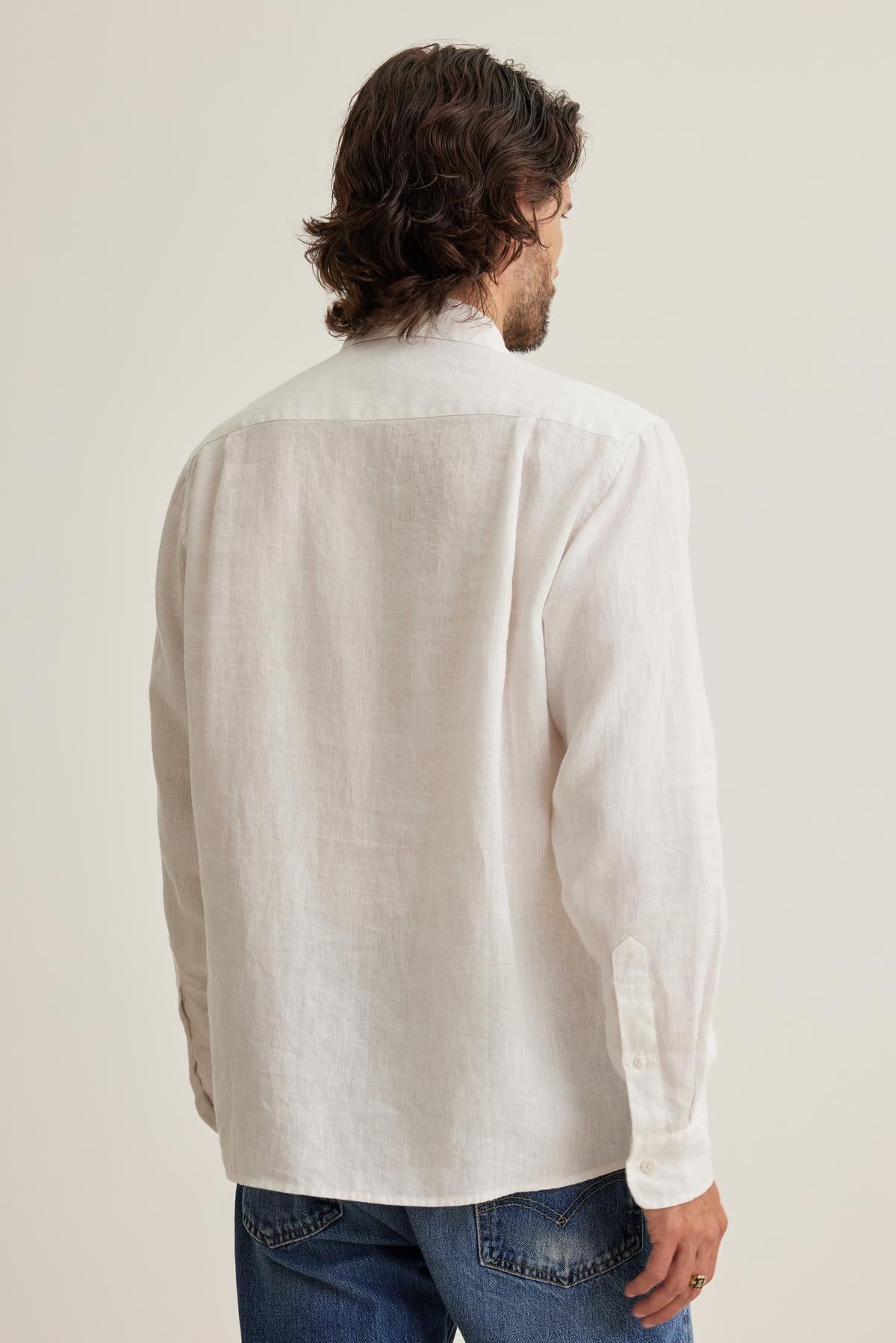   Man with wavy hair in a Velvet by Graham & Spencer CARUSO linen button-up shirt and blue jeans, facing away from the camera. 