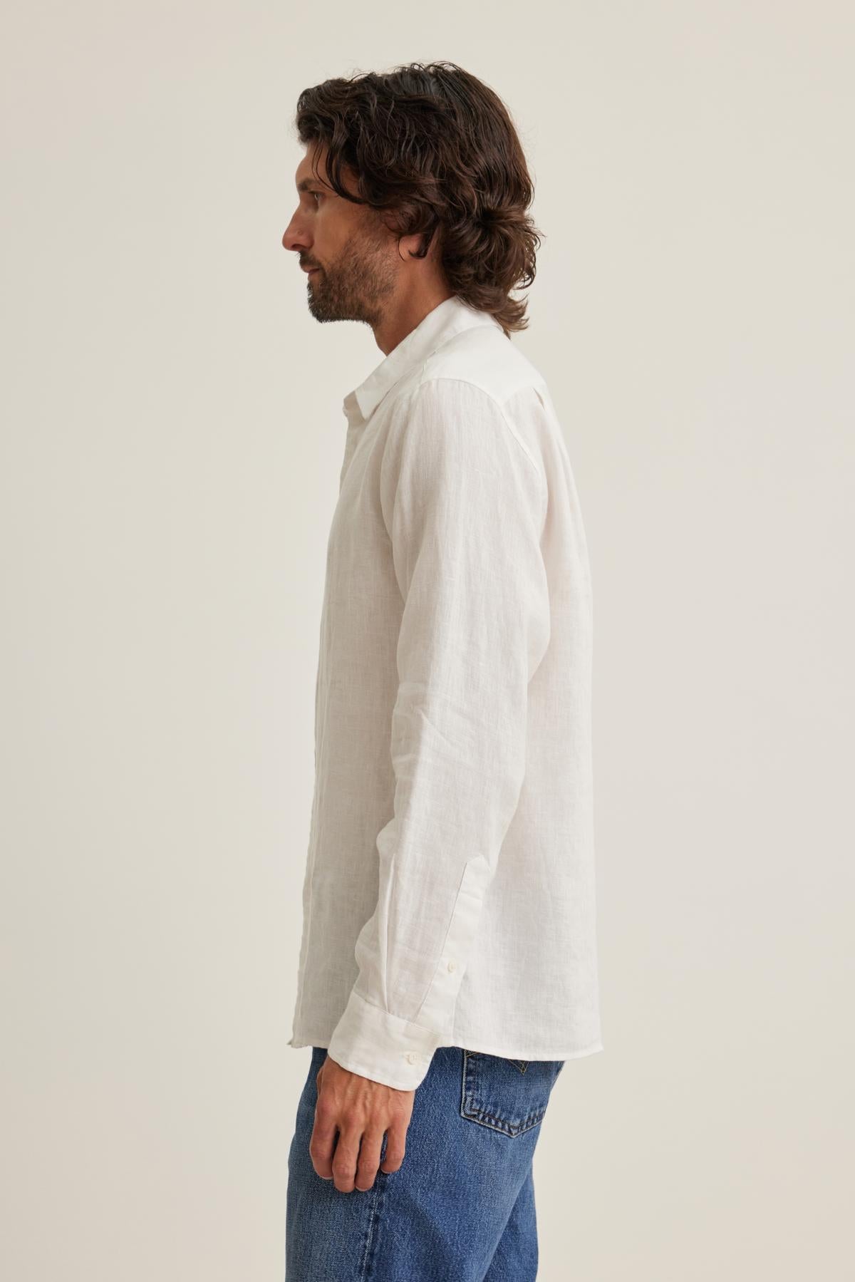   A person with dark hair, wearing a CARUSO LINEN BUTTON-UP SHIRT by Velvet by Graham & Spencer and blue jeans, stands in profile against a plain background. 