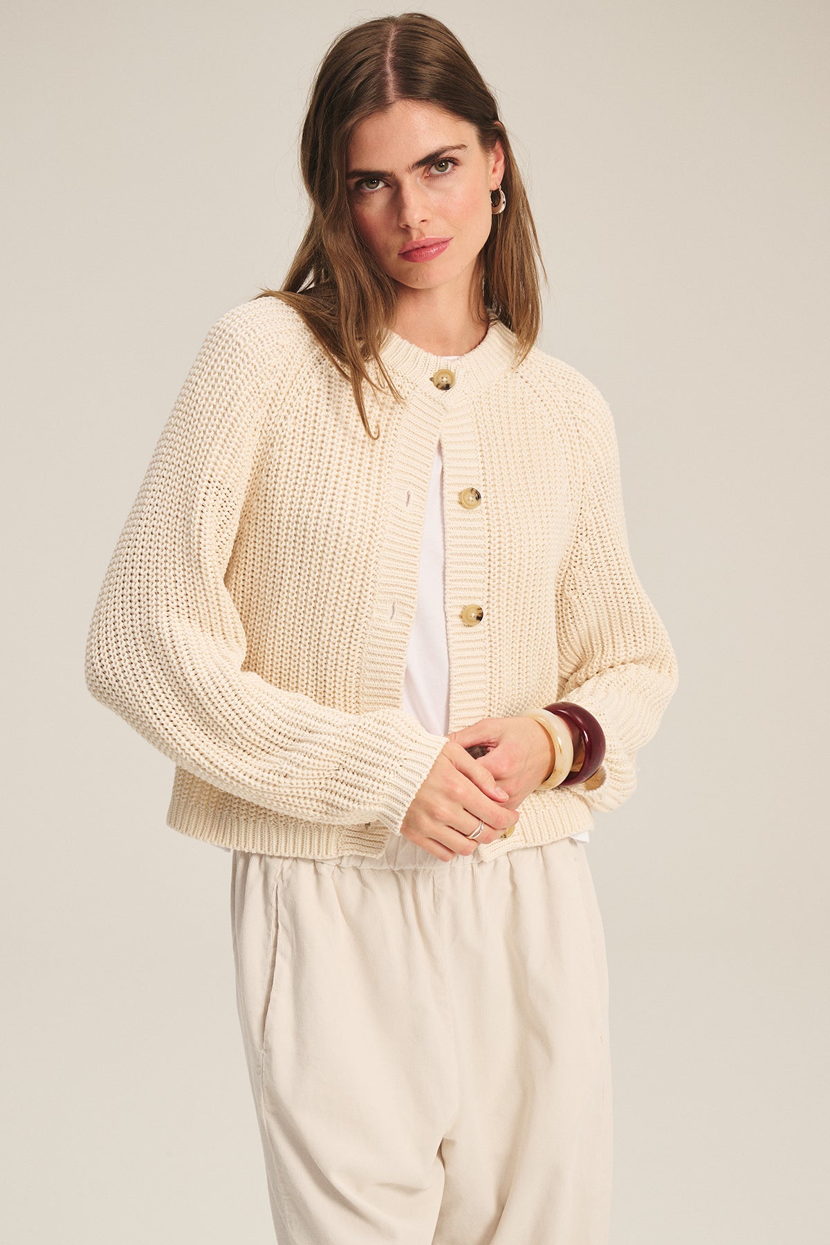 A woman models the Velvet by Graham & Spencer LISABETH CARDIGAN, a chunky cropped layer with large buttons, styled over a white shirt and light pants—an ideal cozy transitional piece for any wardrobe.