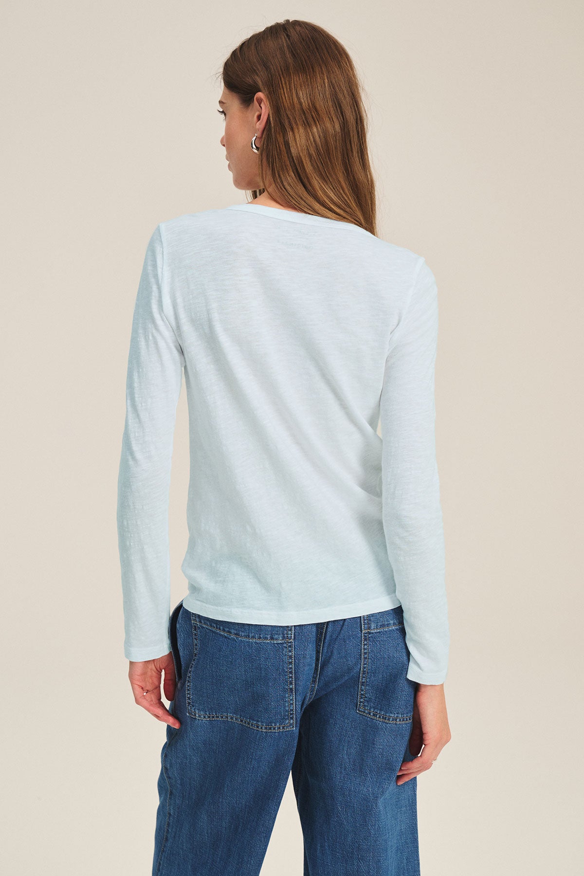A person with long brown hair is seen from the back wearing Velvet by Graham & Spencer’s LIZZIE TEE in light blue textured cotton slub with a crew neckline, paired with blue jeans.-40416944750785