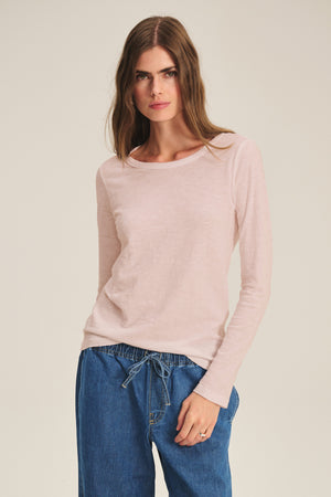 A woman wearing the LIZZIE TEE by Velvet by Graham & Spencer in light pink stands against a plain background, looking at the camera.