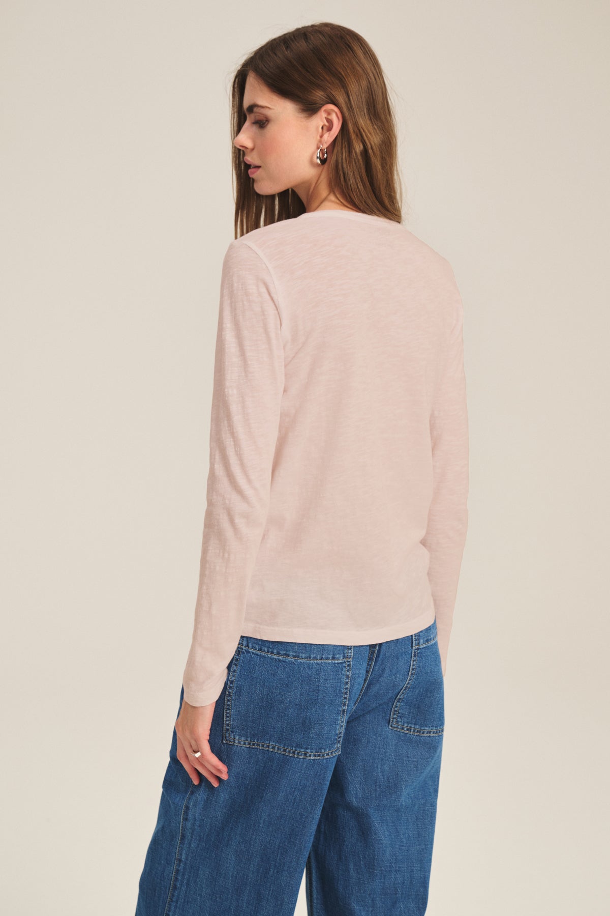 A woman faces away from the camera, wearing the LIZZIE TEE by Velvet by Graham & Spencer in light pink with blue jeans, set against a plain background.-40163417555137