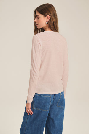 A woman faces away from the camera, wearing the LIZZIE TEE by Velvet by Graham & Spencer in light pink with blue jeans, set against a plain background.
