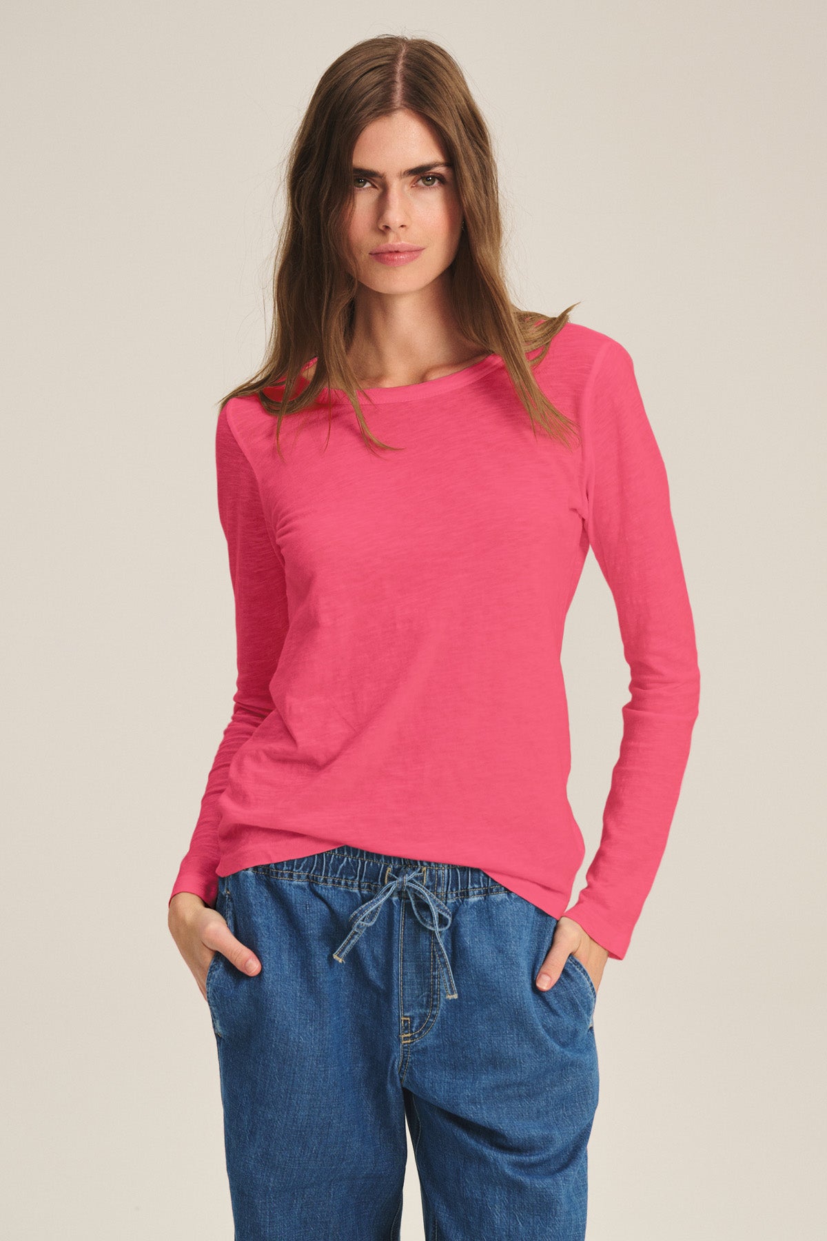 Someone wearing the LIZZIE TEE by Velvet by Graham & Spencer, a long-sleeve cotton slub top with a crew neckline, and blue drawstring pants stands against a plain light background with hands in pockets.-40921275924673