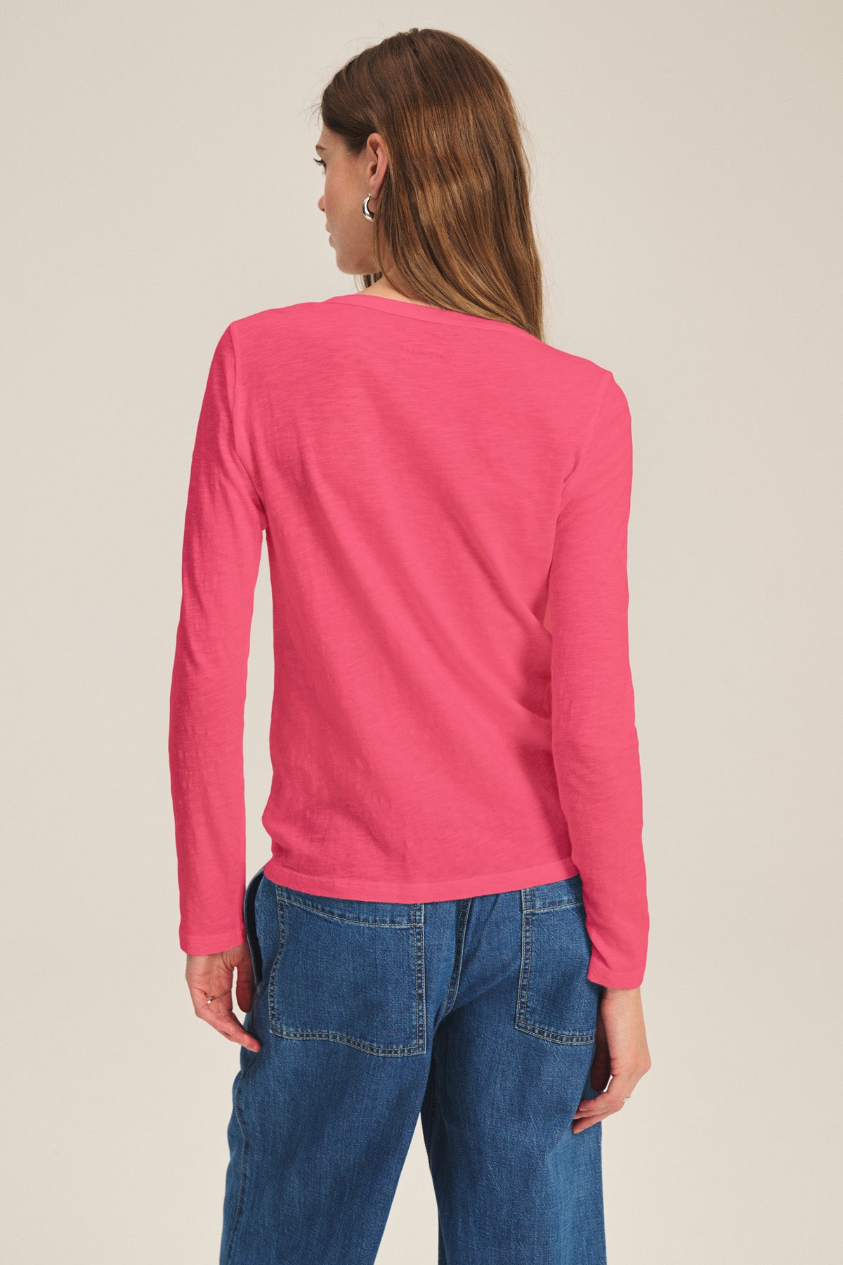 A person with long brown hair is standing with their back to the camera, wearing Velvet by Graham & Spencer's LIZZIE TEE in bright pink and blue jeans.-40921276022977
