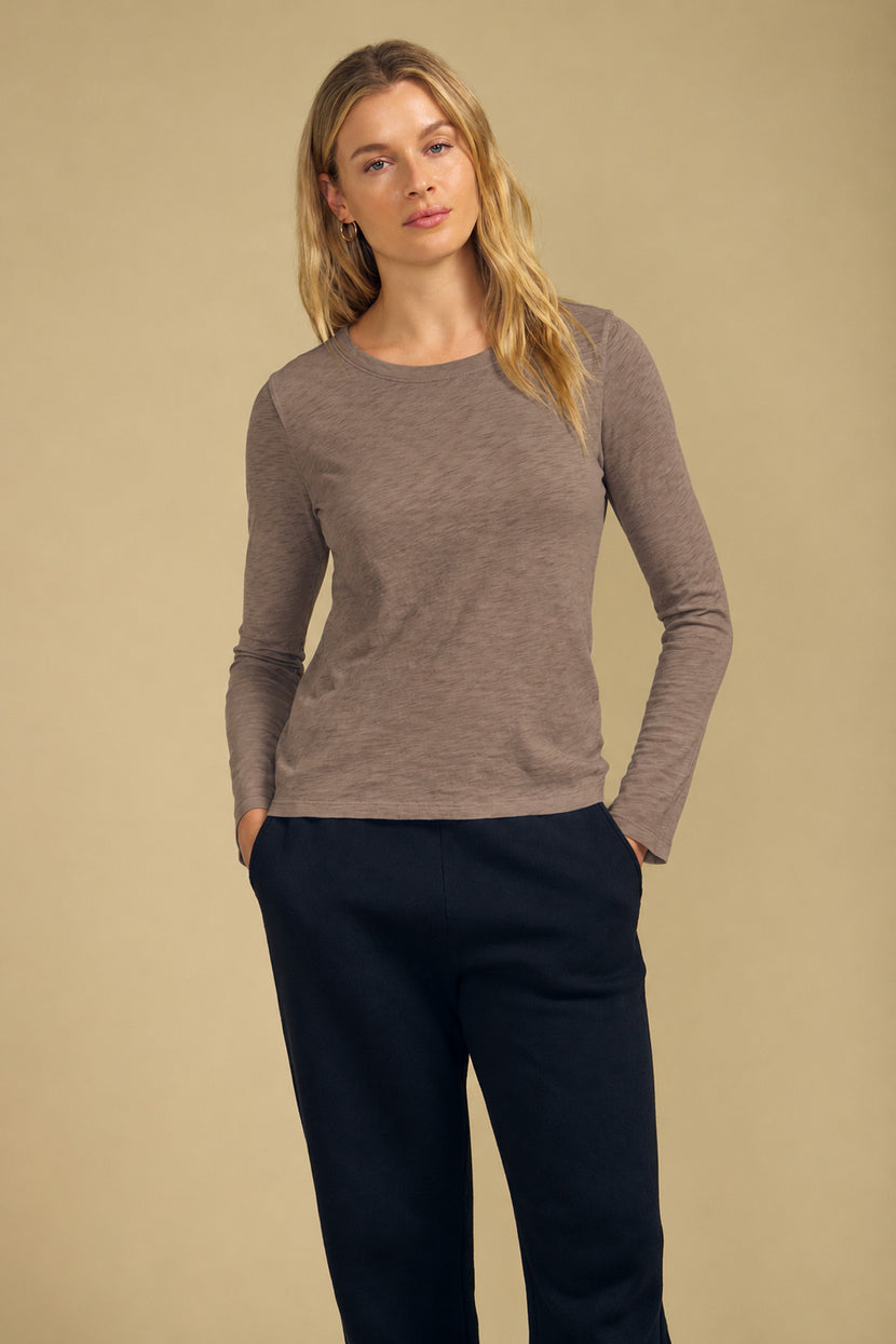 A person wearing a LIZZIE TEE textured cotton slub long-sleeved crewneck t-shirt and dark trousers with hands in pockets.