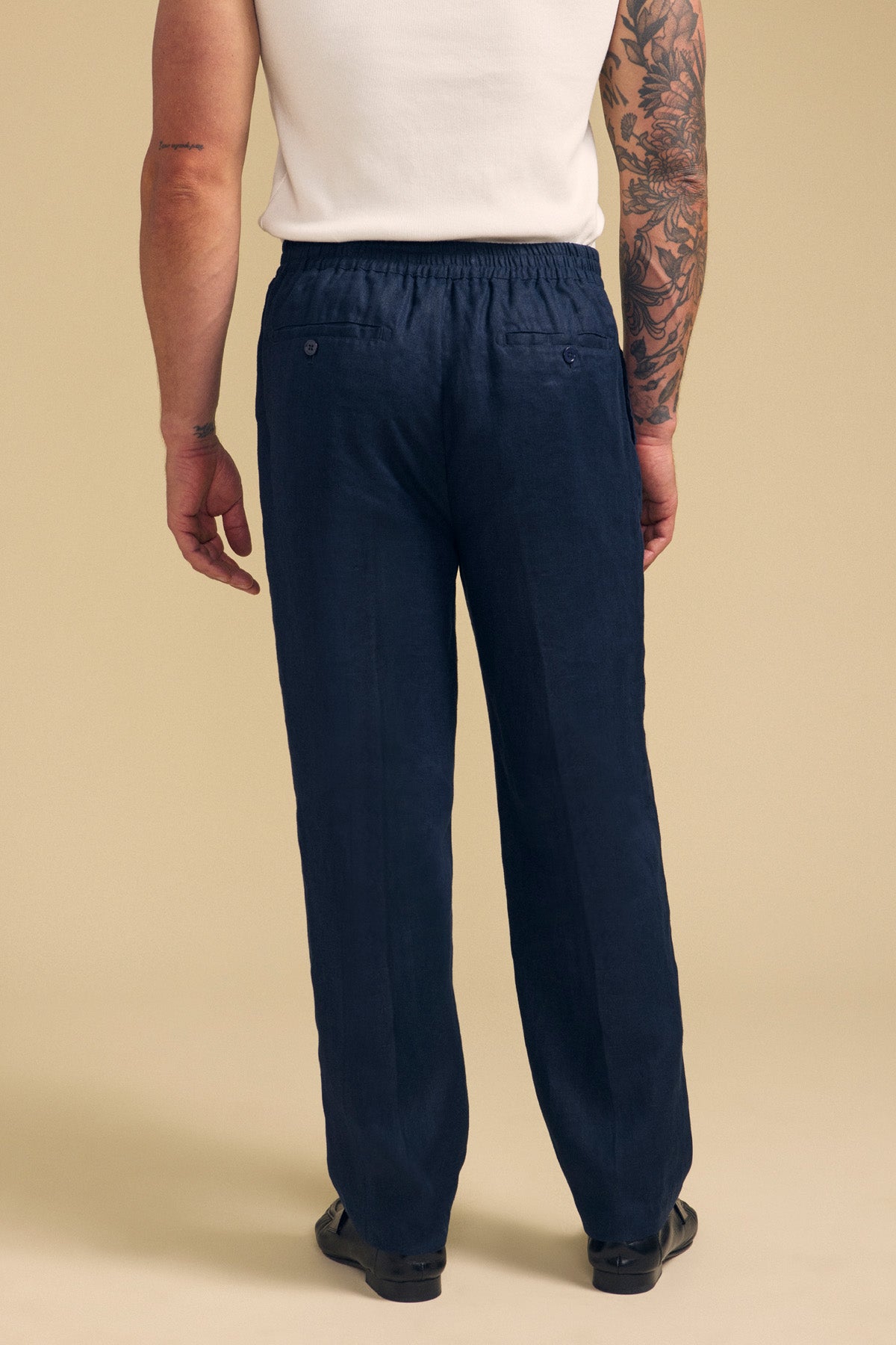 A person wearing a white shirt and Velvet by Graham & Spencer’s ELLIOTT LINEN PANT in navy stands facing away, highlighting the tailored fit, elastic waistband, and two buttoned back pockets.-41701922144449