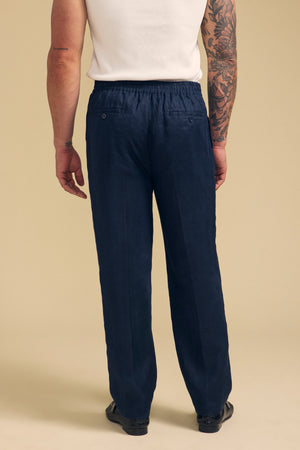 A person wearing a white shirt and Velvet by Graham & Spencer’s ELLIOTT LINEN PANT in navy stands facing away, highlighting the tailored fit, elastic waistband, and two buttoned back pockets.