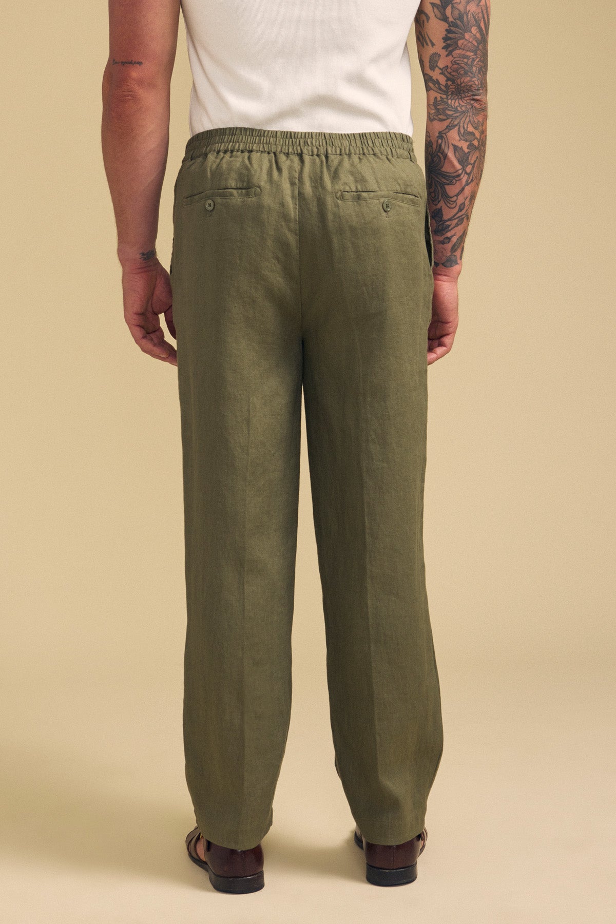 A person is shown from the back against a beige background, wearing Velvet by Graham & Spencer's ELLIOTT LINEN PANT in olive green with sandals.
