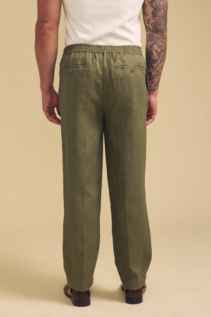 A person is shown from the back against a beige background, wearing Velvet by Graham & Spencer's ELLIOTT LINEN PANT in olive green with sandals.