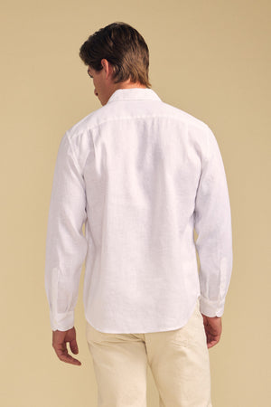 A person stands facing away, wearing the CARUSO LINEN SHIRT by Velvet by Graham & Spencer with light-colored pants against a beige background—ideal for versatile styling.