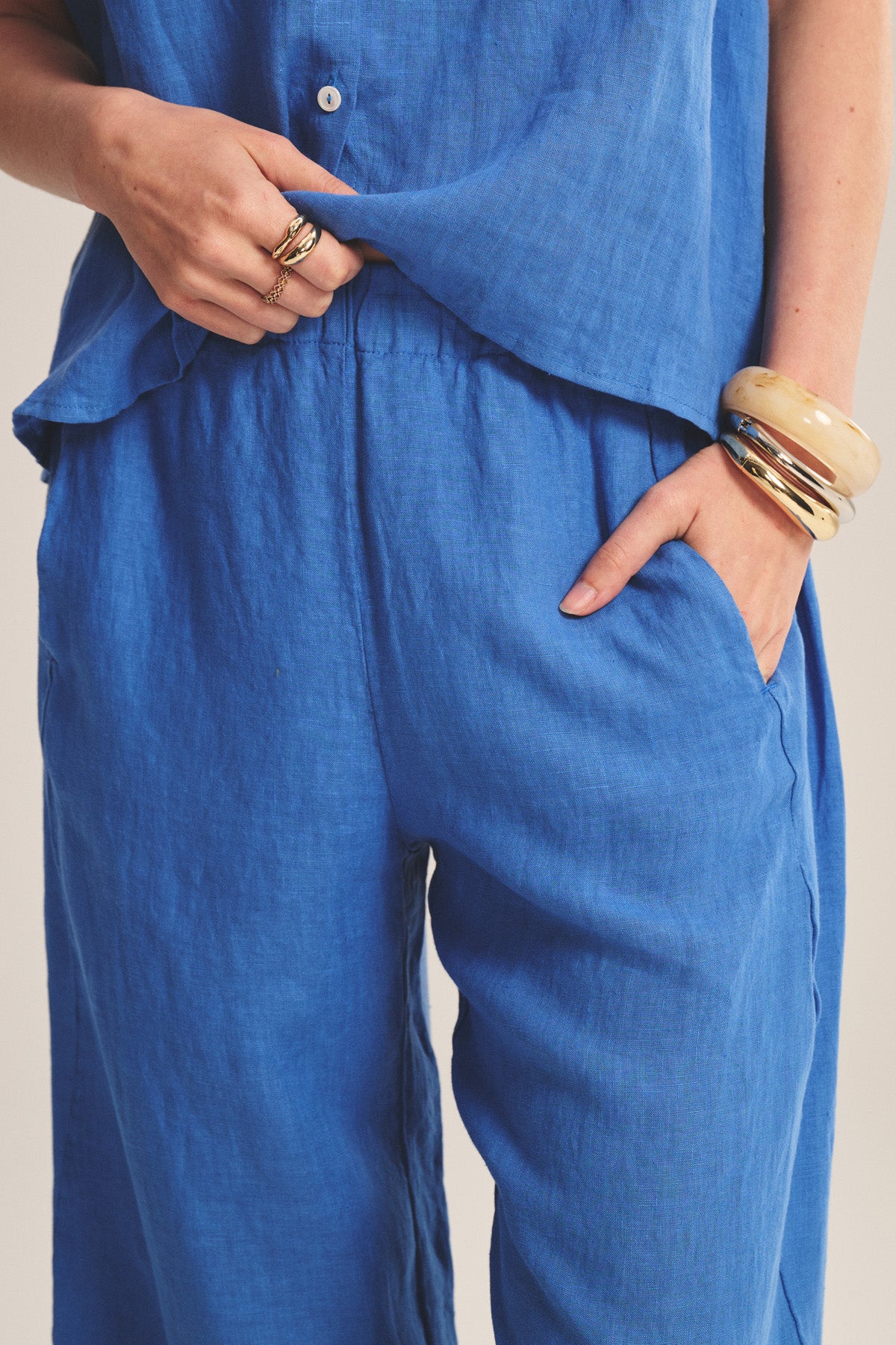 A person in Velvet by Graham & Spencer's LOLA LINEN PANT, styled with one hand in the pocket and the other adjusting their top, accessorized with rings and chunky bangles.-41088950337729