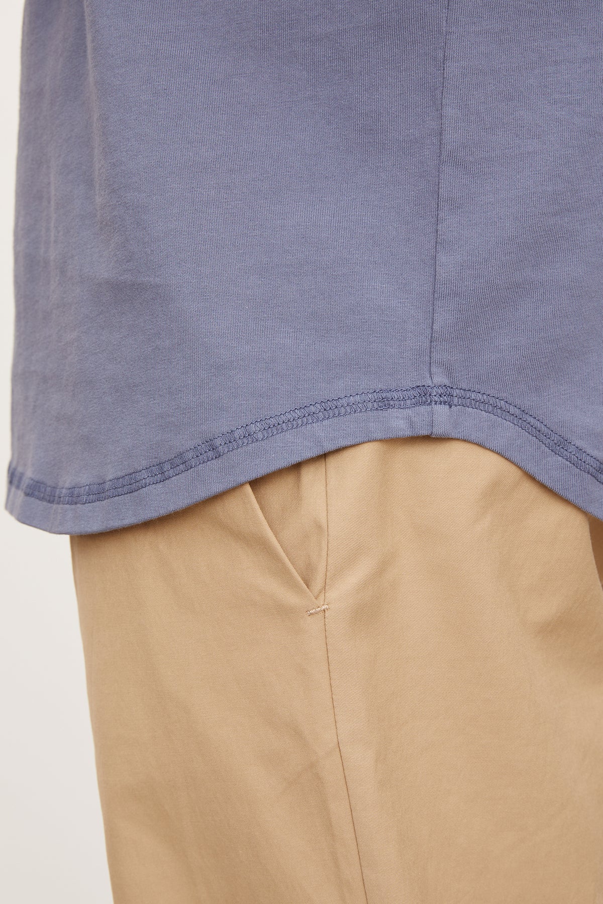 Close-up of a blue cotton knit DEON HENLEY shirt hem over beige trousers, focusing on the fabric and stitching detail by Velvet by Graham & Spencer.-36918612033729