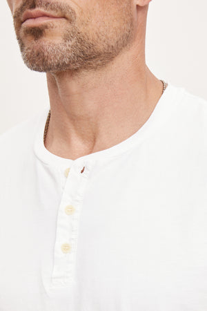 Close-up of a man wearing a white cotton knit Velvet by Graham & Spencer Deon Henley shirt, focusing on the collar and top buttons, with a portion of his neck and chin visible.