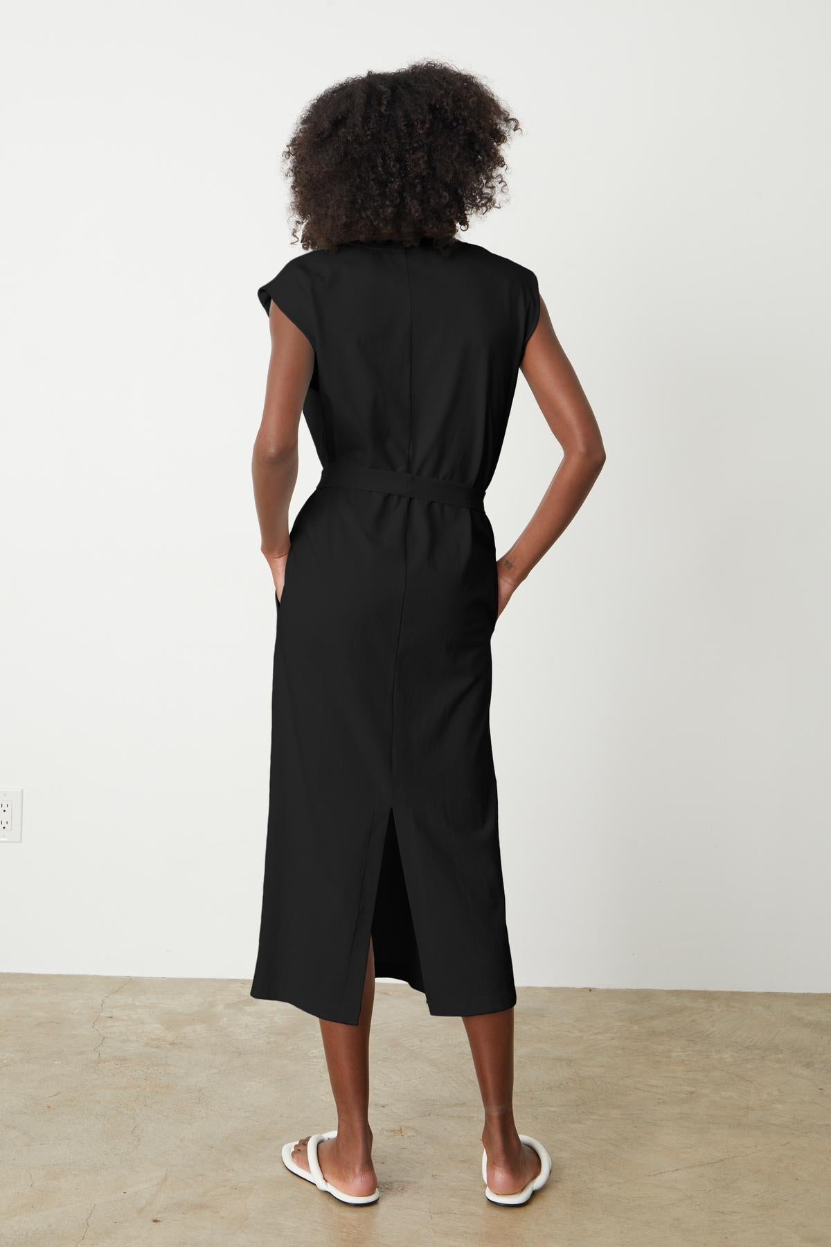   The back view of a woman wearing a Velvet by Graham & Spencer column silhouette midi dress with a detachable belt. 