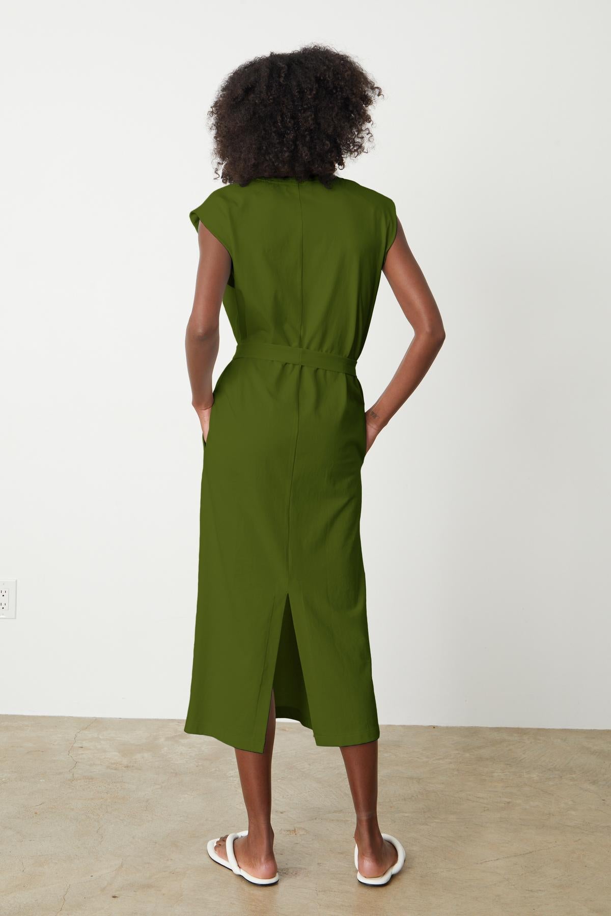   The back view of a woman wearing a green MACI SCOOP NECK DRESS by Velvet by Graham & Spencer with a modern column silhouette and a detachable belt. 