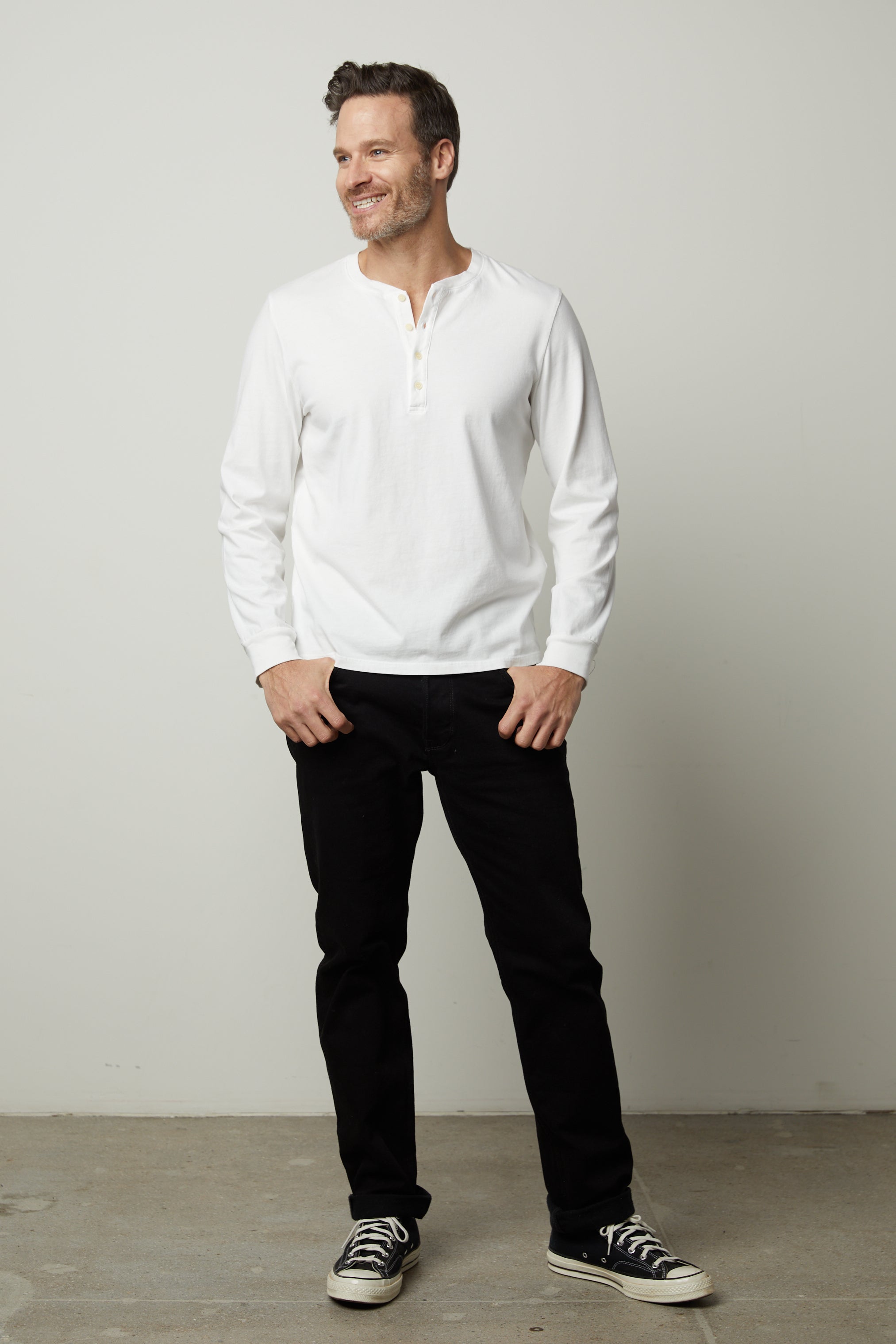   A man wearing a white Velvet by Graham & Spencer REMI HENLEY shirt and black pants. 