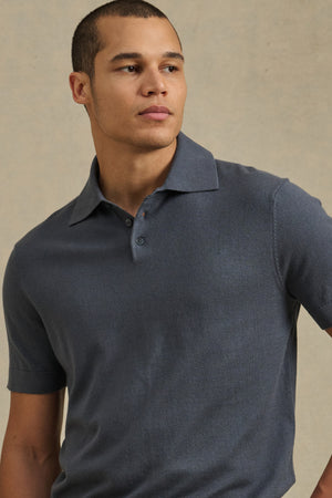 A man wears the Velvet by Graham & Spencer CLYDE SWEATER POLO—a short-sleeved, dark gray lightweight top—standing against a plain, light-colored background.