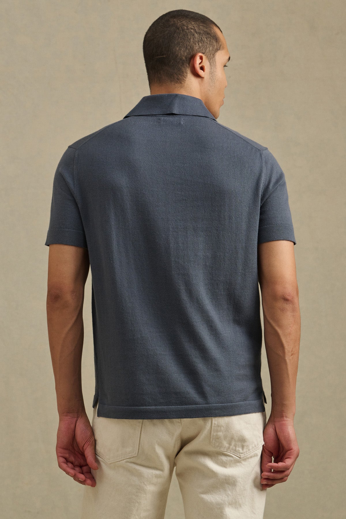 A man faces away from the camera, wearing the Velvet by Graham & Spencer CLYDE SWEATER POLO in dark gray with light pants, set against a plain background.-41428100415681