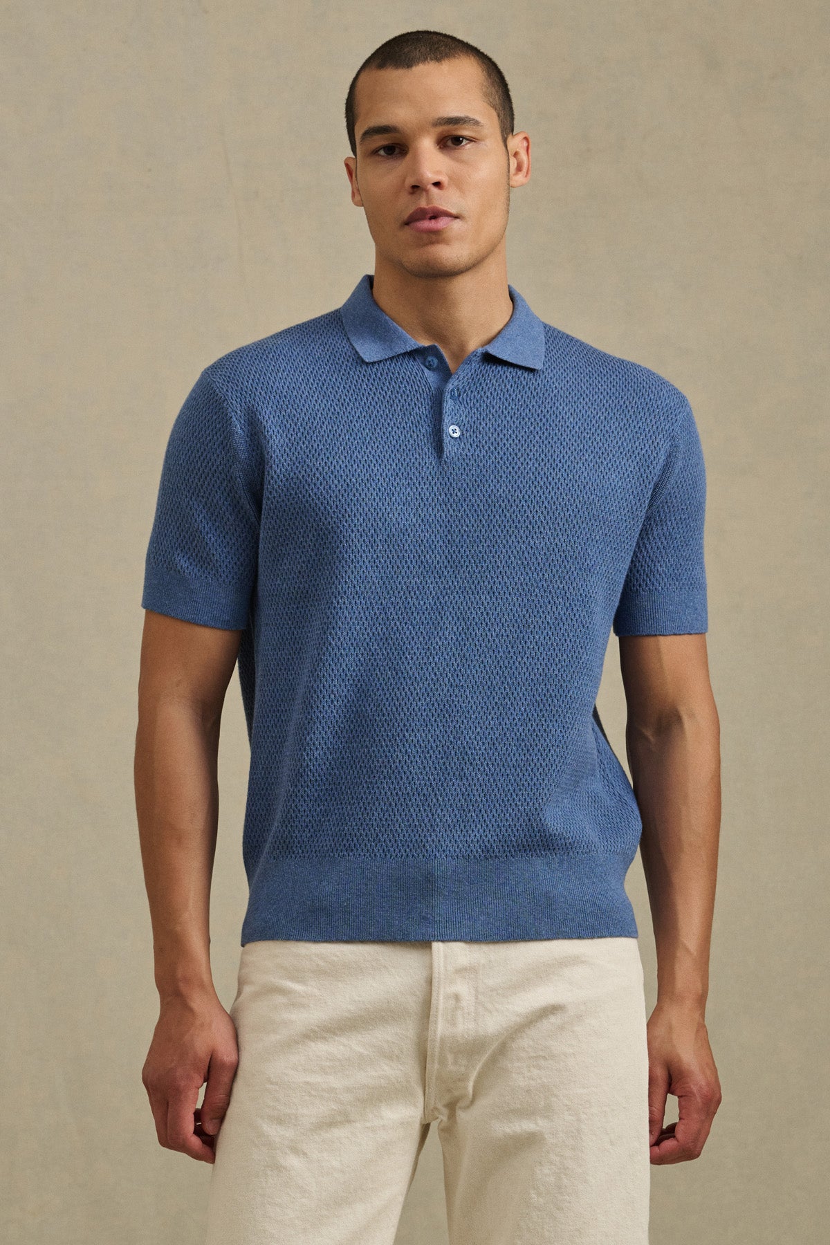 A man stands facing forward against a neutral background, wearing the LOWELL SWEATER POLO by Velvet by Graham & Spencer and off-white pants.