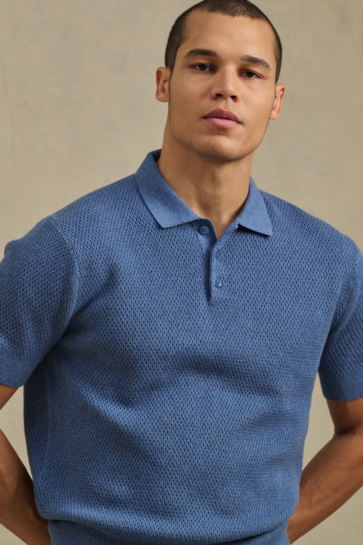 A person wearing the LOWELL SWEATER POLO by Velvet by Graham & Spencer—a textured blue breathable mesh sweater polo—stands in front of a neutral background, looking at the camera.-41145319358657