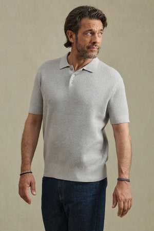 Man wearing the LOWELL SWEATER POLO by Velvet by Graham & Spencer in light gray with dark blue jeans, standing against a plain beige background and looking to his left.