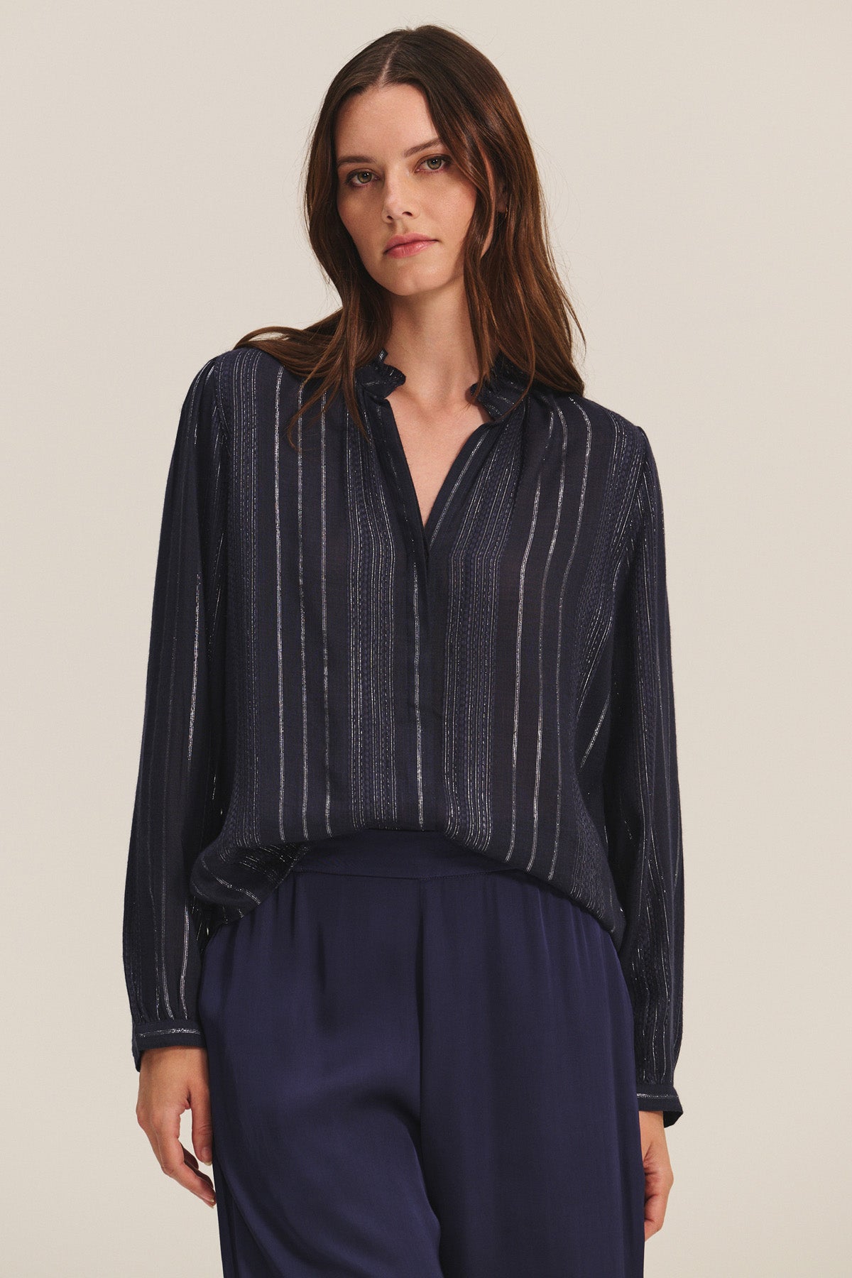 A woman wears the CYNTHIA TOP by Velvet by Graham & Spencer—a navy blue viscose top with vertical lurex weaving—paired with matching navy trousers, standing against a plain light background.-40681606381761