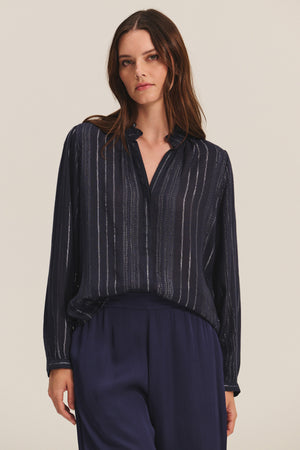 A woman wears the CYNTHIA TOP by Velvet by Graham & Spencer—a navy blue viscose top with vertical lurex weaving—paired with matching navy trousers, standing against a plain light background.