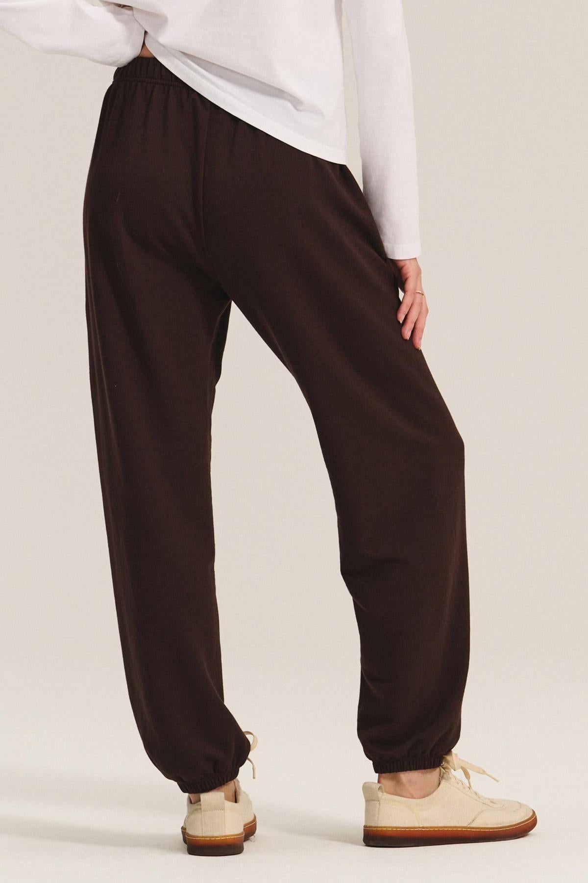 Model wearing EVERS JOGGER by Velvet by Graham & Spencer—relaxed fit black joggers with elastic waist, paired with a white long-sleeve shirt and beige shoes, shown from the back on a light background.-40461949829313