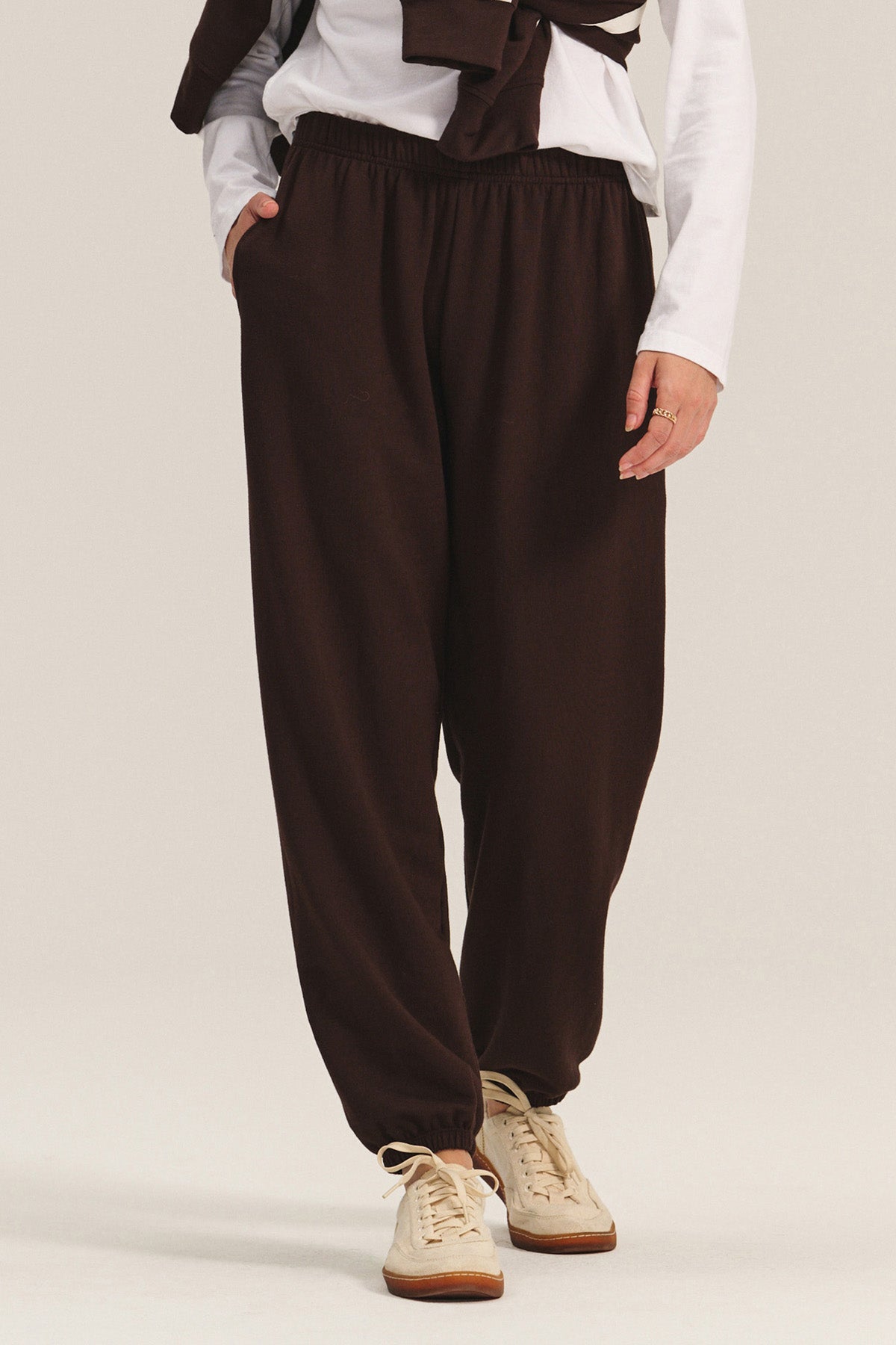 Model in relaxed fit EVERS JOGGER sweatpants by Velvet by Graham & Spencer, featuring an elastic waist, paired with a white long-sleeve shirt and beige sneakers, standing with one hand in the pocket.