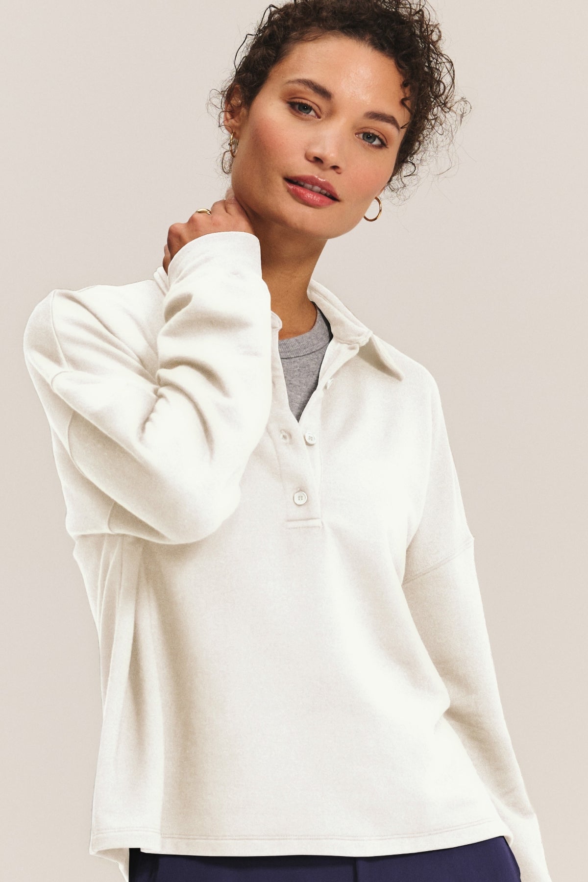 A woman wears the MARIAN SWEATSHIRT by Velvet by Graham & Spencer, a cream long-sleeve top with a collared neckline and buttons, standing against a plain background and looking at the camera.-40740515184833