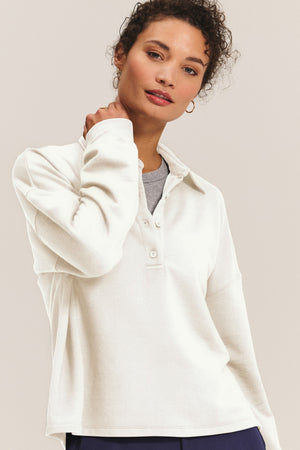 A woman wears the MARIAN SWEATSHIRT by Velvet by Graham & Spencer, a cream long-sleeve top with a collared neckline and buttons, standing against a plain background and looking at the camera.
