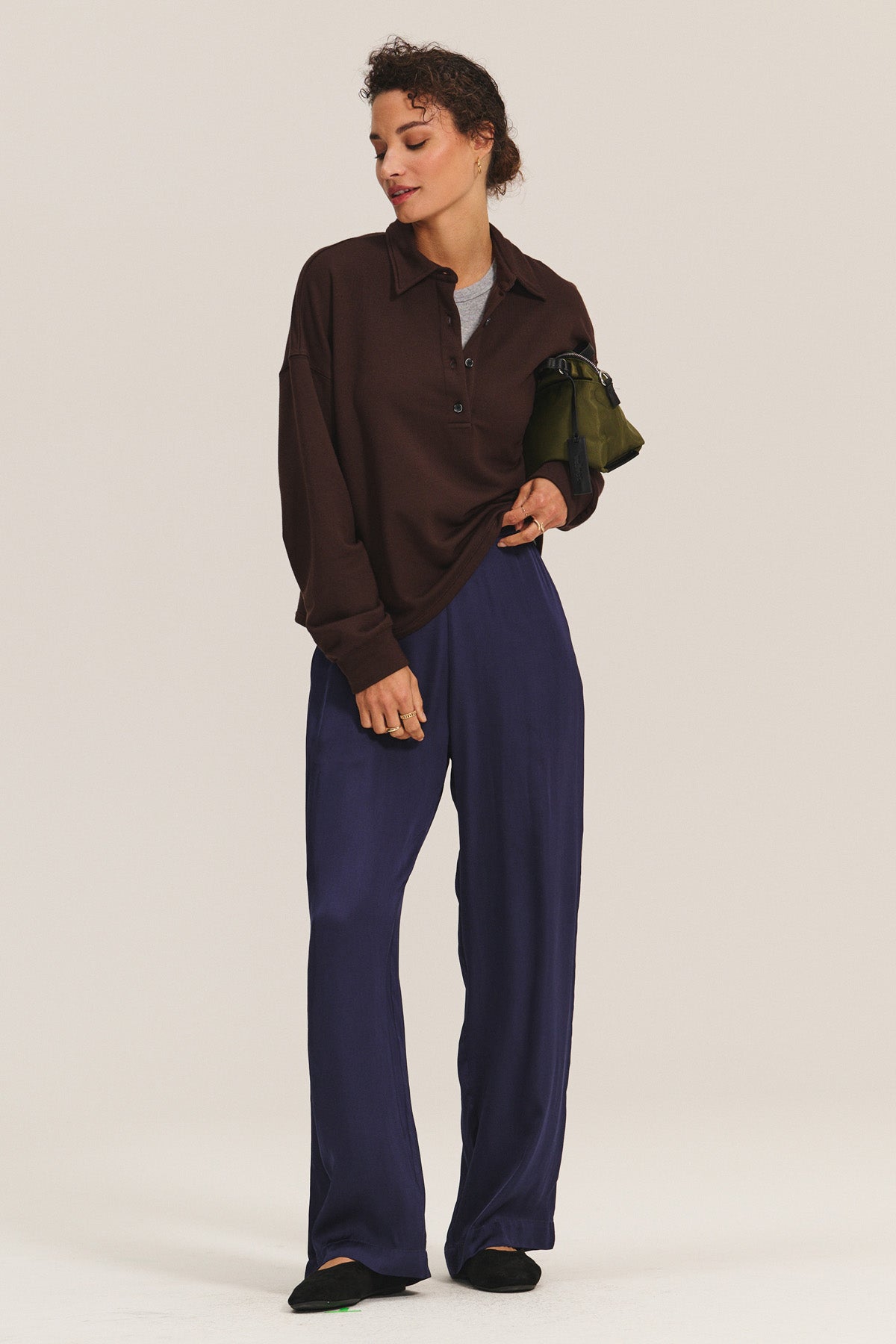 A person stands in a relaxed pose against a plain background, wearing the MARIAN SWEATSHIRT by Velvet by Graham & Spencer, paired with loose navy pants, black shoes, and holding a green bag under their arm.-40598491627713