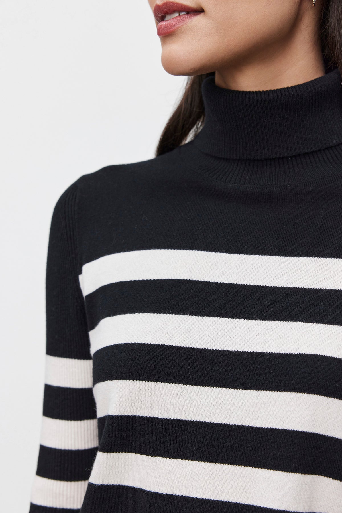   A person wearing the KORIE TURTLENECK SWEATER by Velvet by Graham & Spencer, a luxurious cotton-cashmere blend with black and white stripes, is shown from the shoulders up against a plain background. 