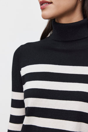 A person wearing the KORIE TURTLENECK SWEATER by Velvet by Graham & Spencer, a luxurious cotton-cashmere blend with black and white stripes, is shown from the shoulders up against a plain background.