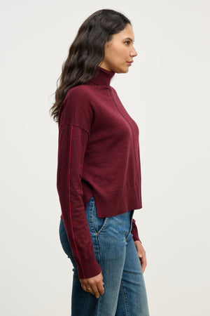 Woman wearing the LIBRA SWEATER by Velvet by Graham & Spencer in a boxy fit turtleneck, paired with blue jeans, standing in profile against a plain light background.