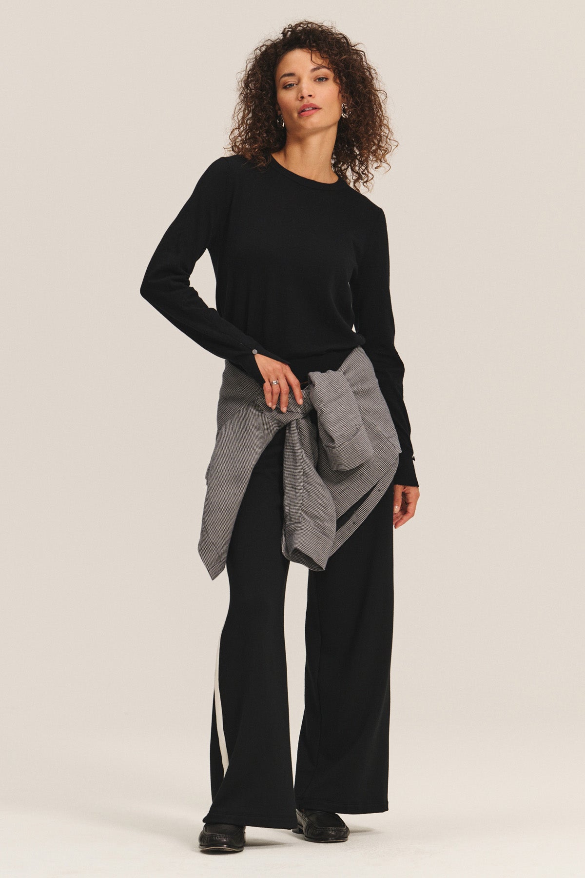 A person stands facing forward in the MELINA SWEATER by Velvet by Graham & Spencer with ribbed trims, paired with black wide-leg pants, black shoes, and a gray jacket tied at the waist against a neutral background.-40461693944001