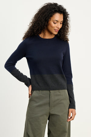 Someone models the ROXY SWEATER by Velvet by Graham & Spencer, featuring a navy and dark gray color-block crew neck in luxe cotton-cashmere, paired with olive green pants, posed against a white background.