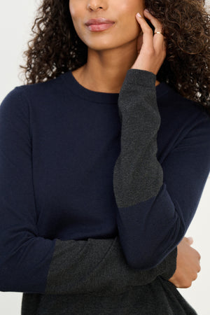 A woman wearing the ROXY SWEATER by Velvet by Graham & Spencer in navy and dark gray colorblock with a crew neckline, touching her face with one hand, shown from shoulders to lips.