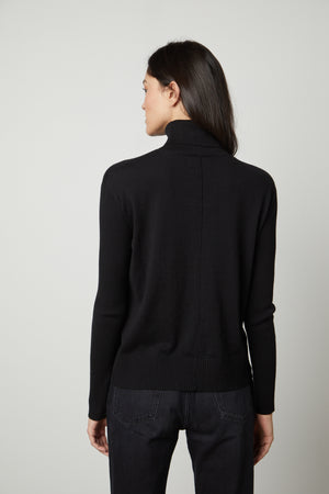 The back view of a woman wearing a fitted black SALLY MOCK NECK SWEATER from Velvet by Graham & Spencer.