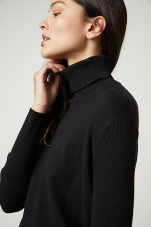 A woman wearing the Velvet by Graham & Spencer SALLY MOCK NECK SWEATER, a black turtle neck cotton-cashmere blend sweater with a ribbed neck.