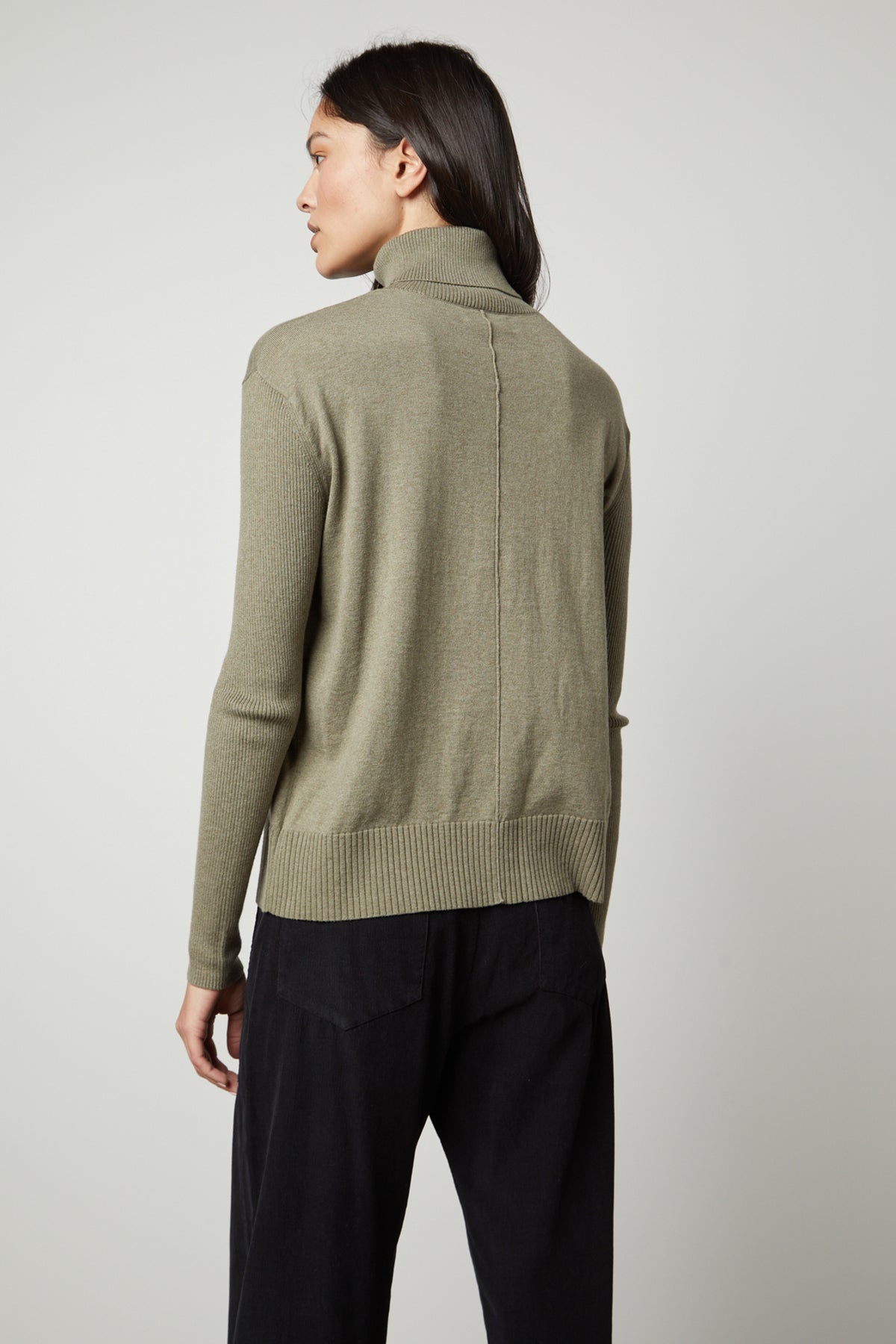   The back view of a woman wearing a ribbed, green SALLY MOCK NECK SWEATER by Velvet by Graham & Spencer. 
