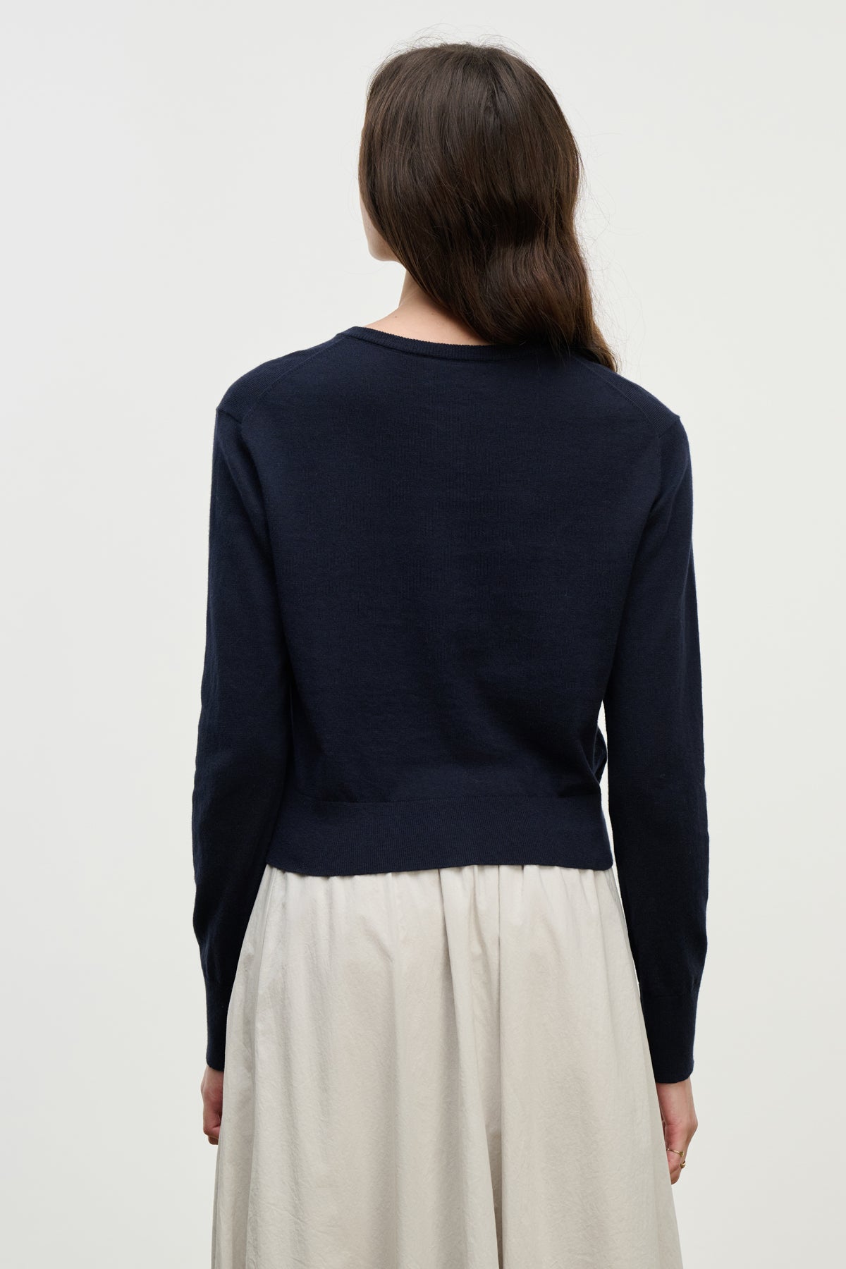 A person with long brown hair is shown from the back against a plain light background, wearing the VIOLETTE CARDIGAN by Velvet by Graham & Spencer in navy blue cotton cashmere and an off-white skirt.-39800434622657